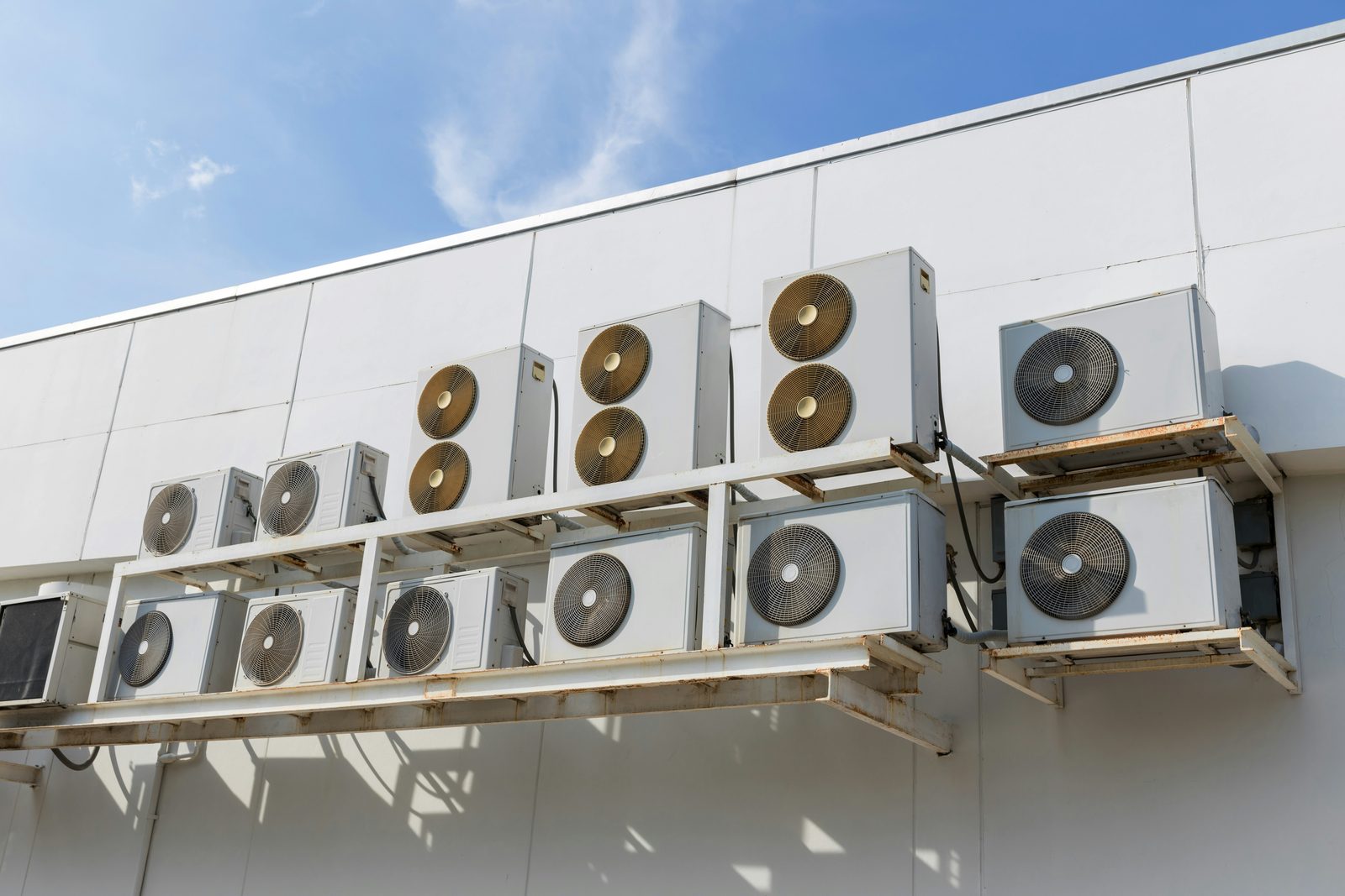 Bank of commercial HVAC condenser units mounted on a building against a blue sky